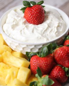 a bowl of whipped cream surrounded by sliced pineapple and strawberries