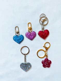 four different colored heart shaped keychains on a white surface with one holding a pair of scissors