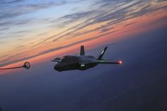 a fighter jet flying through the air at dusk with its landing gear down and lights on