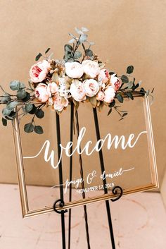 a welcome sign with flowers and greenery is displayed on a metal easel for an outdoor wedding