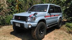 a blue suv parked in front of some trees and bushes on the side of a dirt road