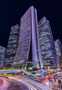 the city is lit up at night with many tall buildings in the foreground and cars on the street below