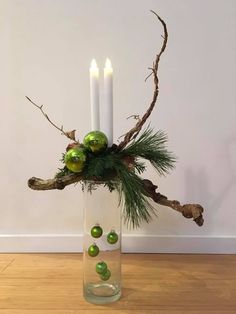 a glass vase filled with green ornaments and two lit candles on top of a wooden floor