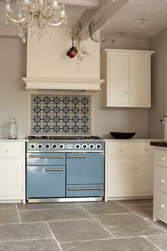 a blue stove top oven sitting inside of a kitchen next to white cabinets and drawers