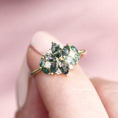 a close up of a person's hand holding a ring with green and white stones