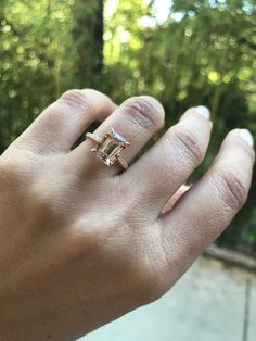 a person's hand with a ring on it and trees in the back ground