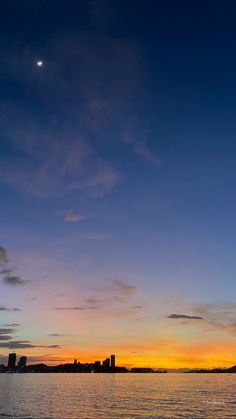 the sun is setting over the water with buildings in the distance and clouds in the sky