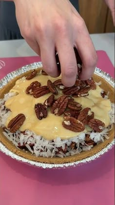 a person placing pecans on top of a pie with icing and coconut flakes