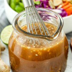 a glass jar filled with dressing next to a bowl of vegetables