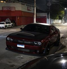 a red car parked on the side of a road at night with other cars in the background