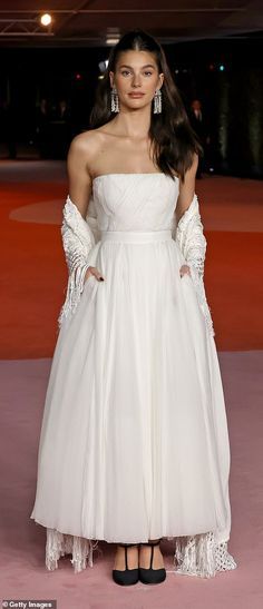 a woman in a white dress standing on a pink carpet with her hands on her hips