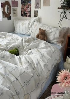 a teddy bear sitting on top of a bed in a room with white sheets and pillows