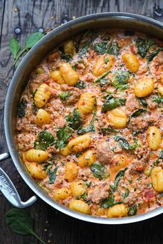 a pot filled with pasta and spinach on top of a wooden table