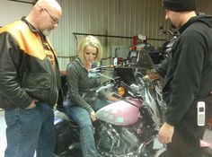 two men and a woman looking at a motorcycle