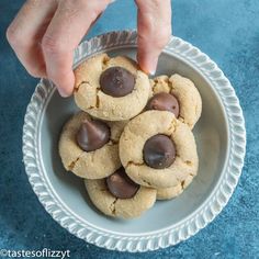 a person is picking up some cookies from a bowl on a blue tablecloth surface