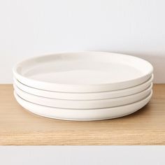 four white plates stacked on top of each other in front of a white wall and wooden table