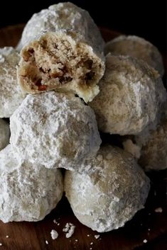 a pile of snowball cookies sitting on top of a wooden cutting board with powdered sugar