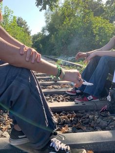 two people sitting on train tracks with their feet crossed and one person holding something in his hand