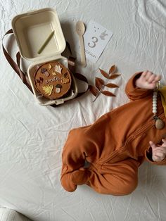 a baby laying on its back next to some food and spoons in a box