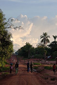 several people walking down a dirt road with trees in the background