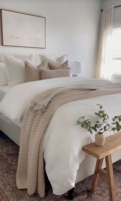 a bed with white linens and pillows in a bedroom next to a wooden bench