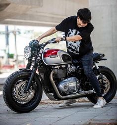 a man sitting on top of a motorcycle parked in front of a building with his hand on the handlebars