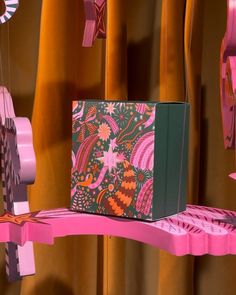 a pink and green box sitting on top of a shelf next to some decorations hanging from the ceiling