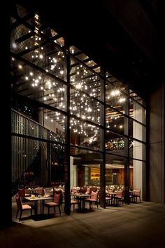 the inside of a restaurant with tables and chairs lit up by lights hanging from the ceiling