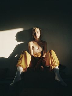 a woman sitting on the floor with her legs crossed, wearing yellow pants and socks