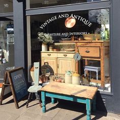 an antique and antiques store front with wooden furniture in the display window, including a small blue table