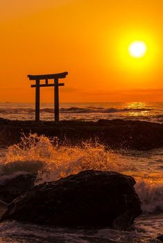 the sun is setting over an ocean with waves crashing in front of a small structure