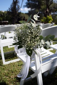 a bunch of white chairs sitting in the grass with flowers on them and ribbons tied to them