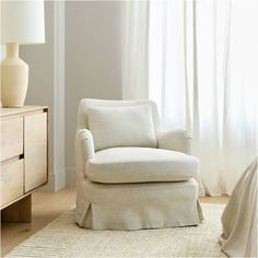 a white chair sitting on top of a rug next to a dresser and lamp in a room