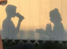 two people sitting on the ground with their shadows cast by them and one person holding a cell phone up to his ear