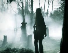 a person standing in front of a cemetery on a foggy day with trees and tombstones