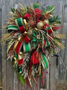 a christmas wreath hanging on the side of a wooden fence with red, green and gold ribbons