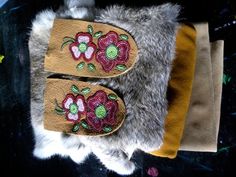 two pairs of slippers with flowers on them are sitting on a fur rug next to a pair of gloves