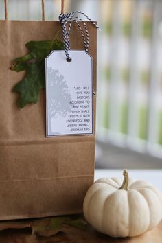 a small white pumpkin sitting next to a brown paper bag with a tag on it