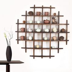 a wooden shelf with cups and vases on it next to a table in front of a white wall