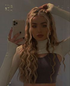 a woman with long curly hair is taking a selfie in front of a mirror