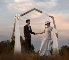 a man and woman standing next to each other in front of a wooden arch holding hands