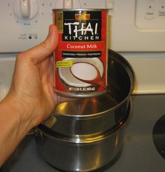 a can of coconut milk is being held in front of a stove top burner