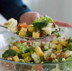 a person holding a spoon full of broccoli salad