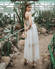 a woman wearing a white dress standing in front of cacti