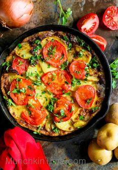 a pizza in a pan with tomatoes and other vegetables around it on a table next to potatoes