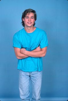 a man standing with his arms crossed in front of a blue background wearing jeans and a t - shirt