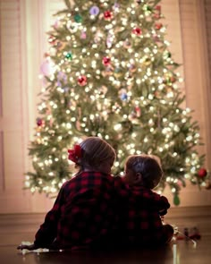 two children sitting in front of a christmas tree