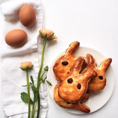 two buns shaped like rabbits on a plate next to some flowers and an egg