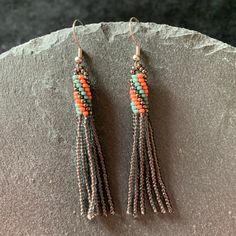 two pairs of beaded earrings with tassels on top of a stone slab