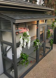 a caged in area with flowers and plants on the outside, along side a building